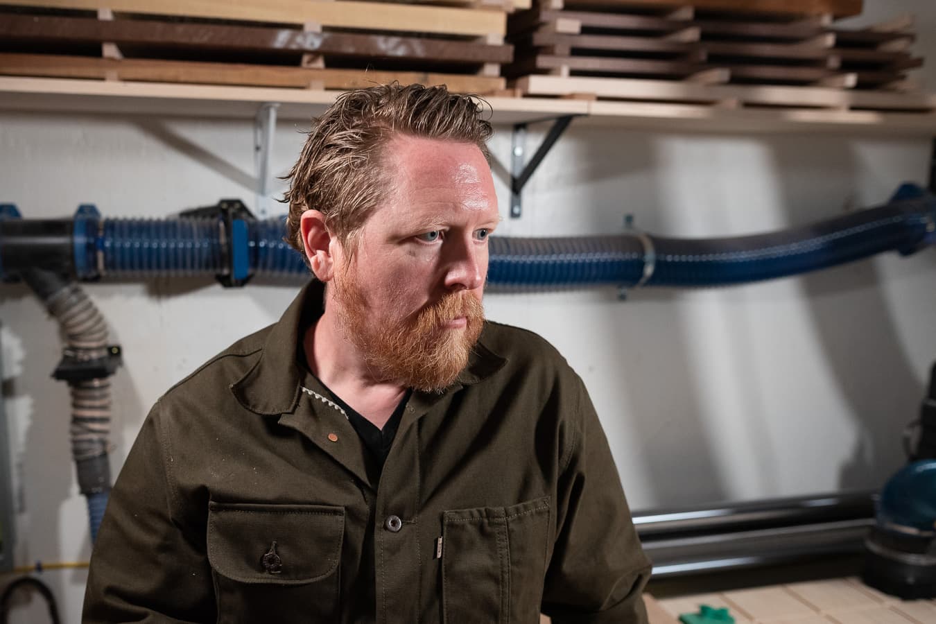 Christopher in the shop, lumber racked on the wall behind him
