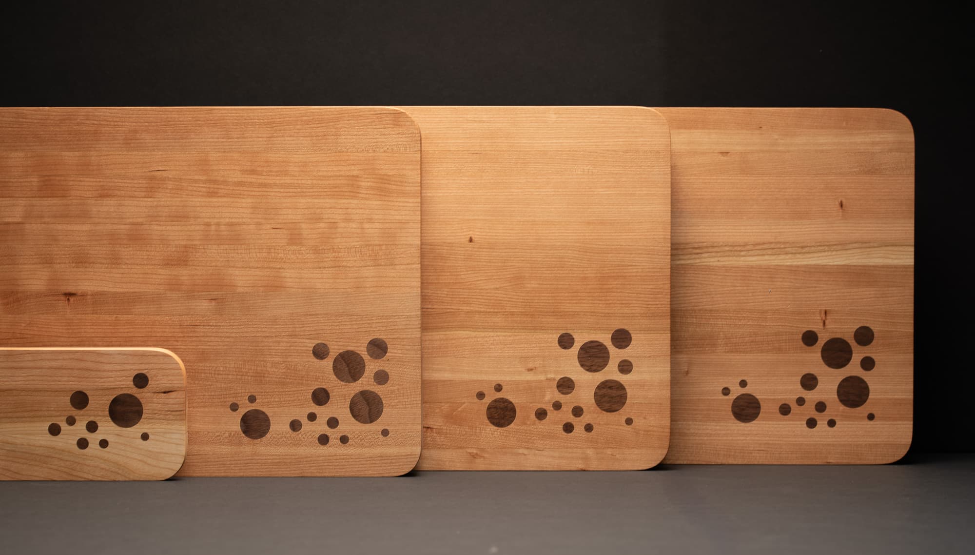 Four cherry boards from the edition, largest to smallest, each carrying the same walnut circle inlay